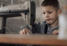 Chłopiec szyje w domu przy maszynie do szycia vintage